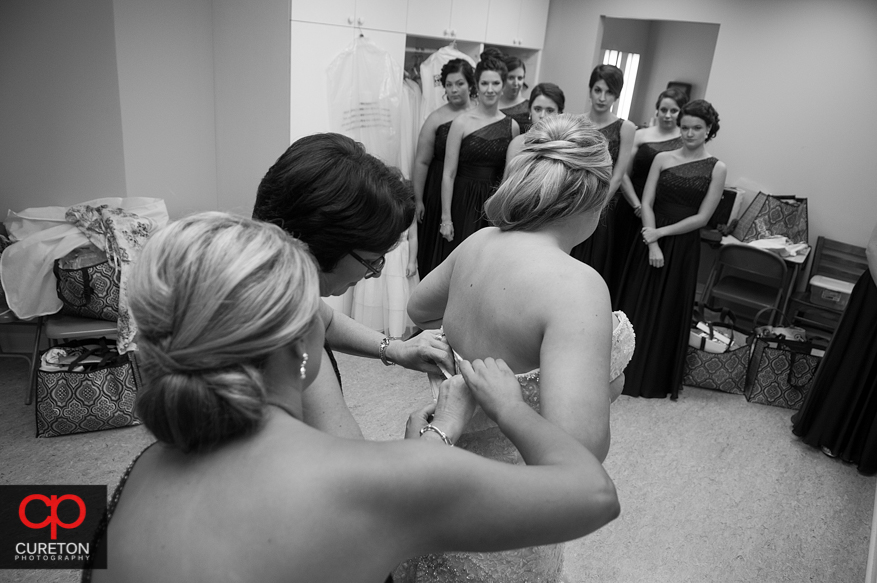 Bridesmiads help the bride into her dress.