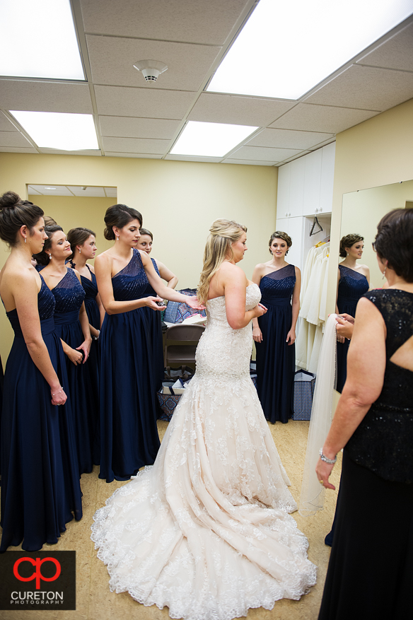Bridesmiads help the bride into her dress.