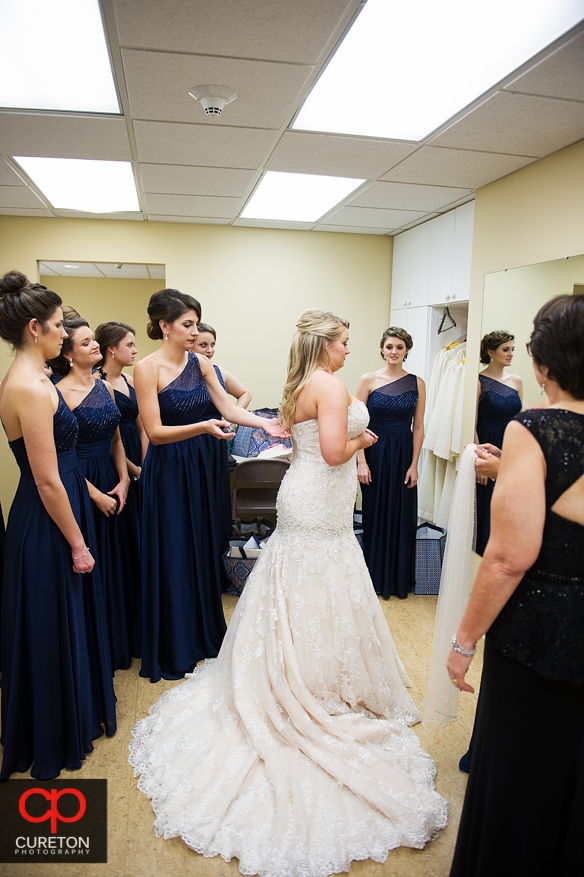 Bridesmiads help the bride into her dress.