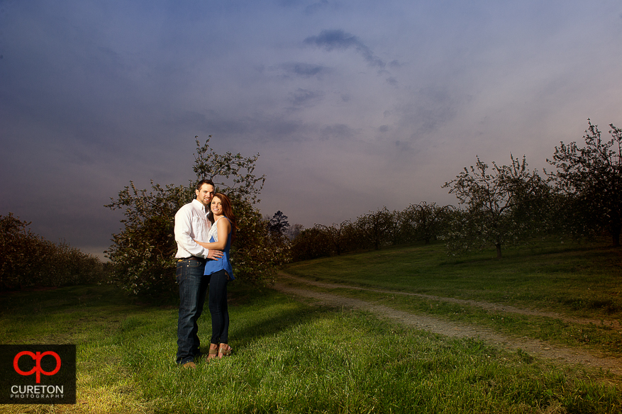 Engaged couple in an apple orchard with a pretty sky.