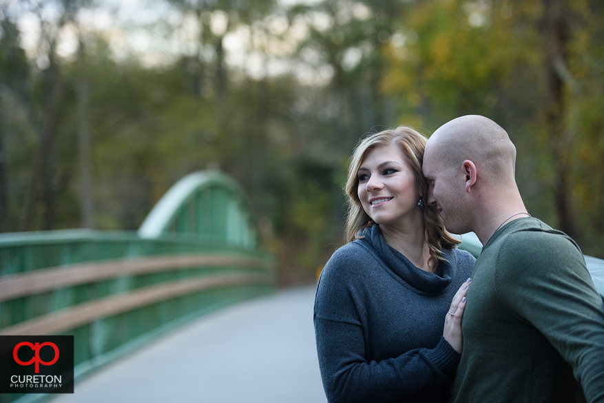 Engaged couple snuggling on a bridge.