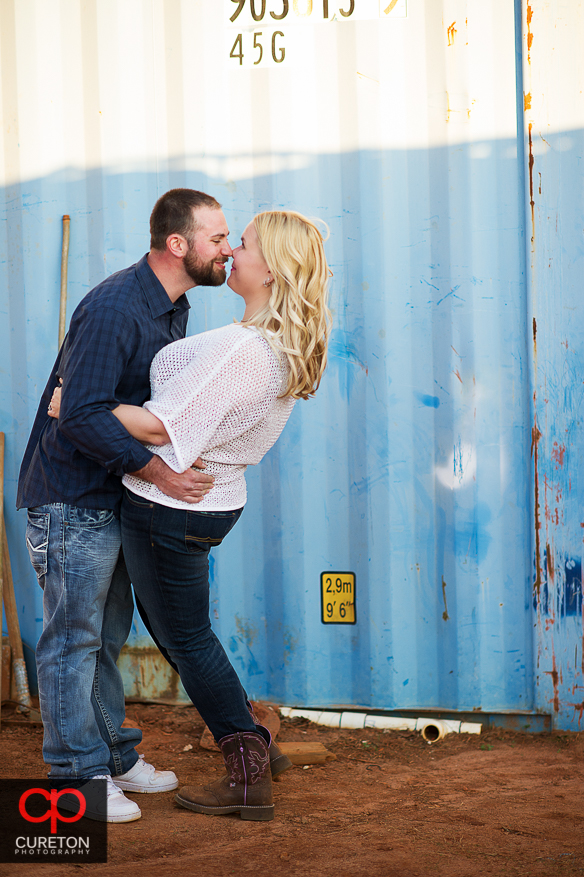 Groom kissing his fiancee in front of a storage container.