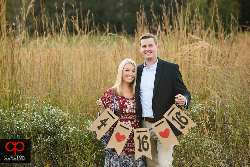 Couple holding up a cute pennant sign at a Botanical Garden engagement session in Clemson,SC..