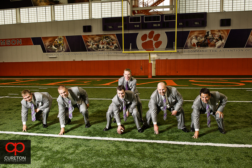 Groom and his groomsmen playing football on the field at the Clemson indoor football complex.