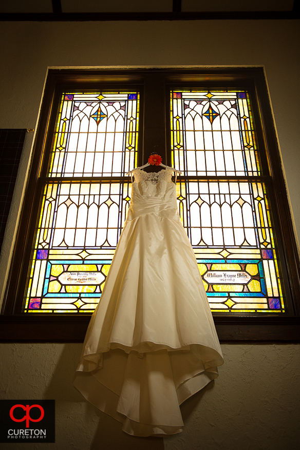 Bride's dress hanging in front of a stained glass window.