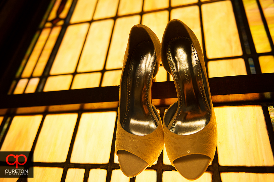 The bride's shoes hanging in front of a stained glass church window.