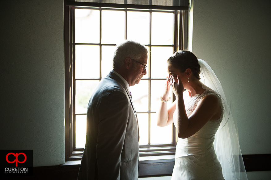 The bride wipes tears from her eyes as her dad sees her for the first time.