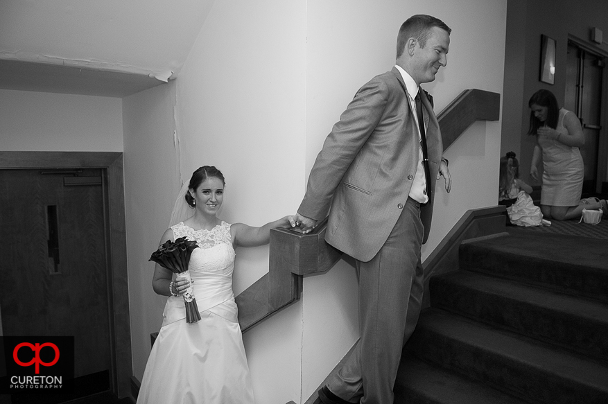 The bride and groom hold hands around a corner before the wedding.