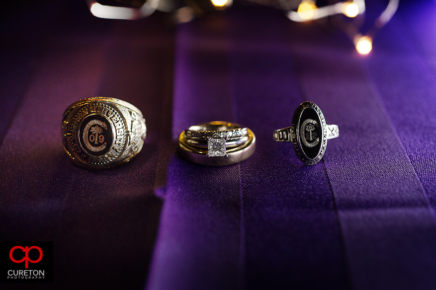 Creative shot of the bride and grooms wedding rings and Clemson college rings.