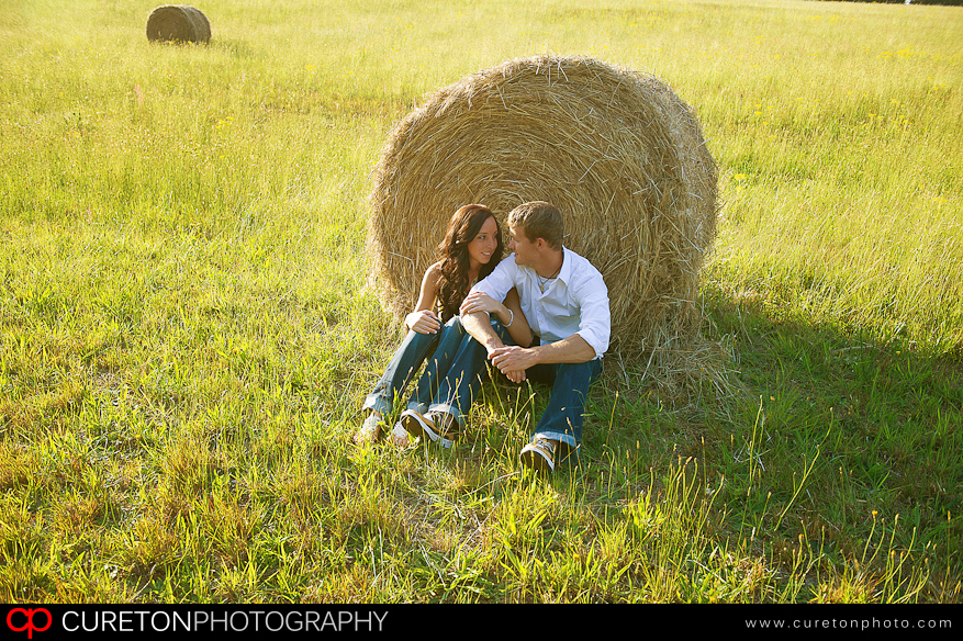 A couple cuddled up in front of a hay bale.