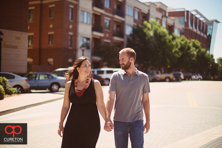 Couple walking the streets of downtown during a pre wedding engagement session at Falls Park on the Reedy in Greenville,SC.