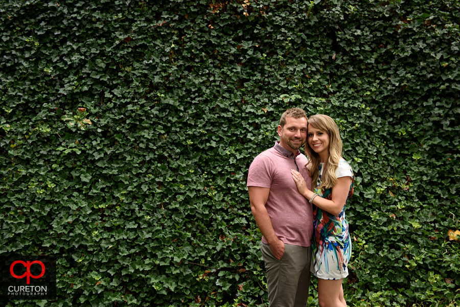Engaged couple posing in front of a wall of ivy.