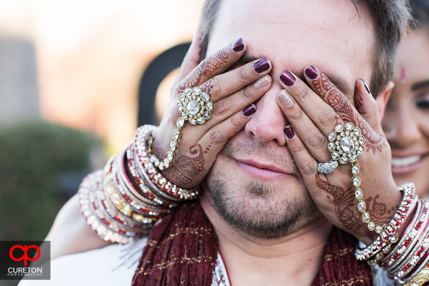 Bride covering grooms eyes showing her elaborate jewelry,