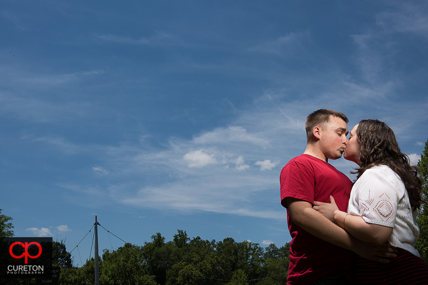 Engaged couple kissing with beautiful blue sky background.