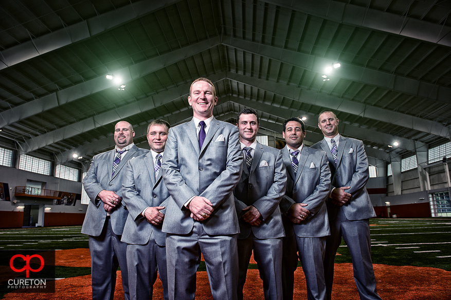 Groom and his groomsmen posing on the fifty yard line of the Clemson indoor football complex.