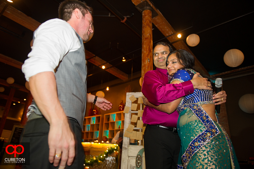 Bride and groom hugging bride's cousin after he gave a toast.