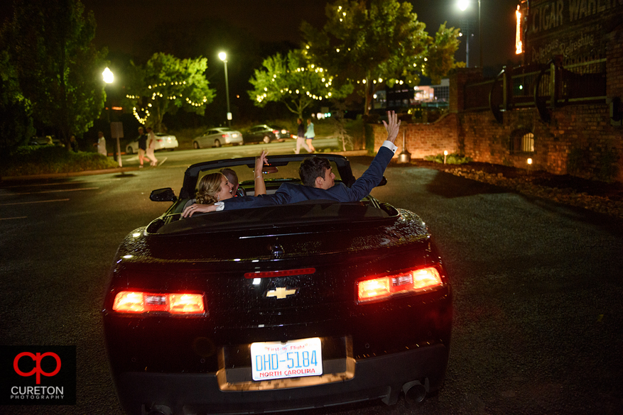 Wedding couple waiving from a convertible Camaro.