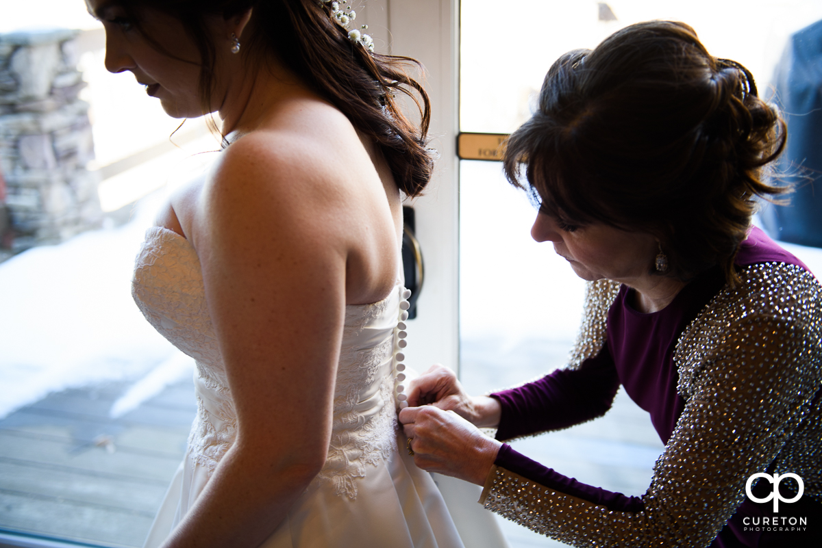 Bride's mother buttoning the back of her dress.