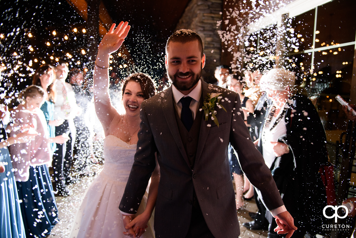 Married couple making a grand exit as the guests throw fake snow at the reception.