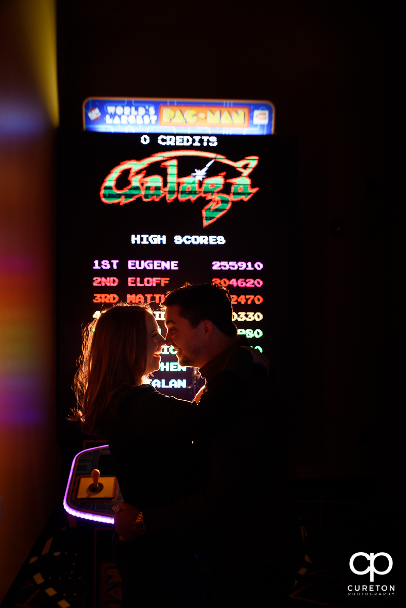 Man and his fiancee dancing in front of the world's largest Pac Man at their arcade engagement session at Spare Time in Greenville,SC.