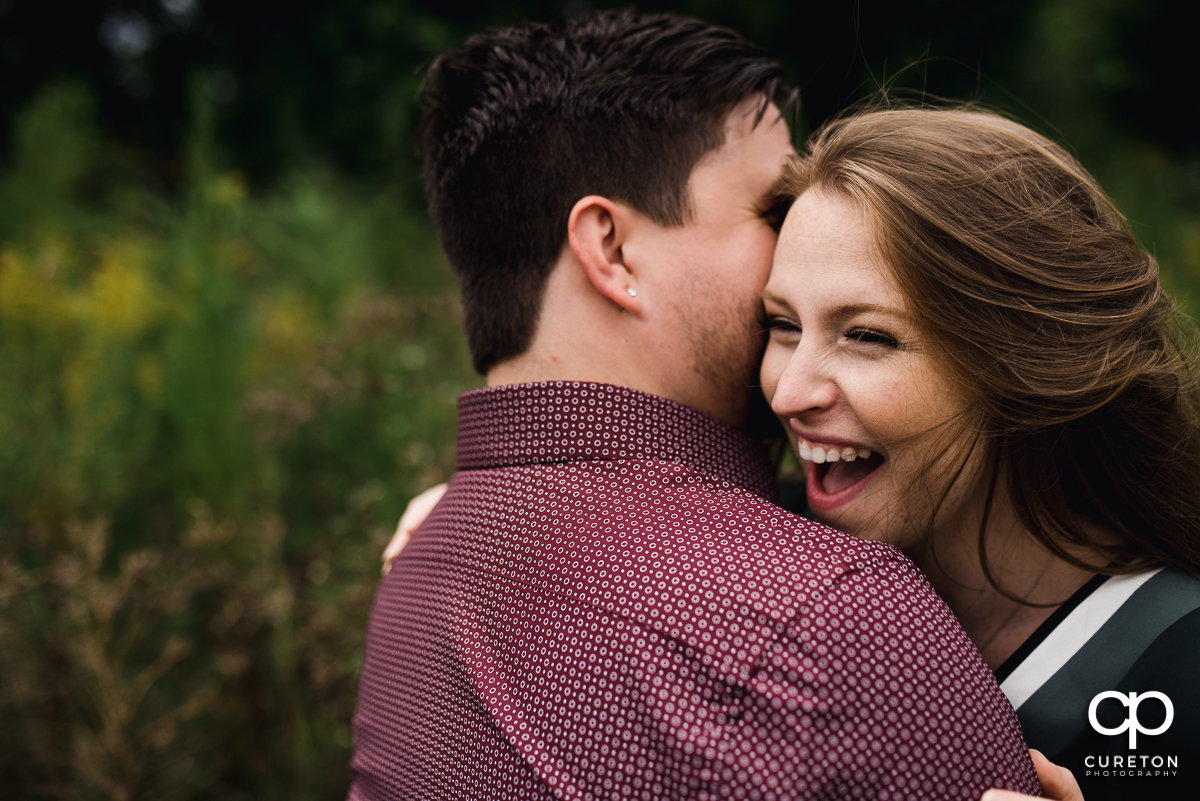 Woman laughing as her fiancee whispers into her ear.