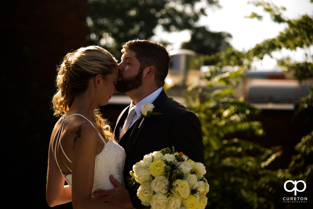 Groom kissing his bride on the forehead after their Artisan Traders wedding.