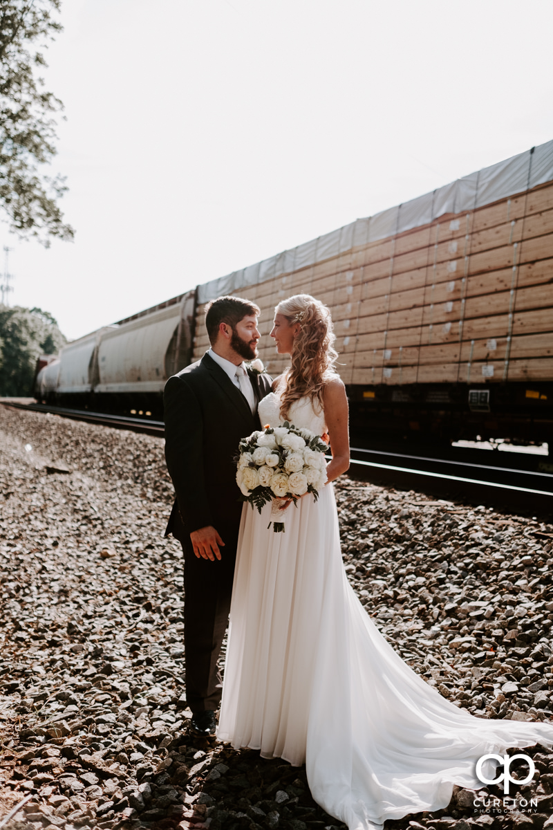 Bride and groom standing beside a train track.
