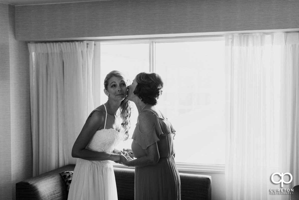 Bride's om kissing her daughter in the cheek as she gets ready for her wedding.