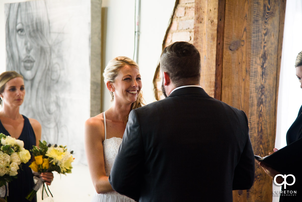 Bride smiling at her groom during their wedding ceremony at Artisan Traders in Greenville.