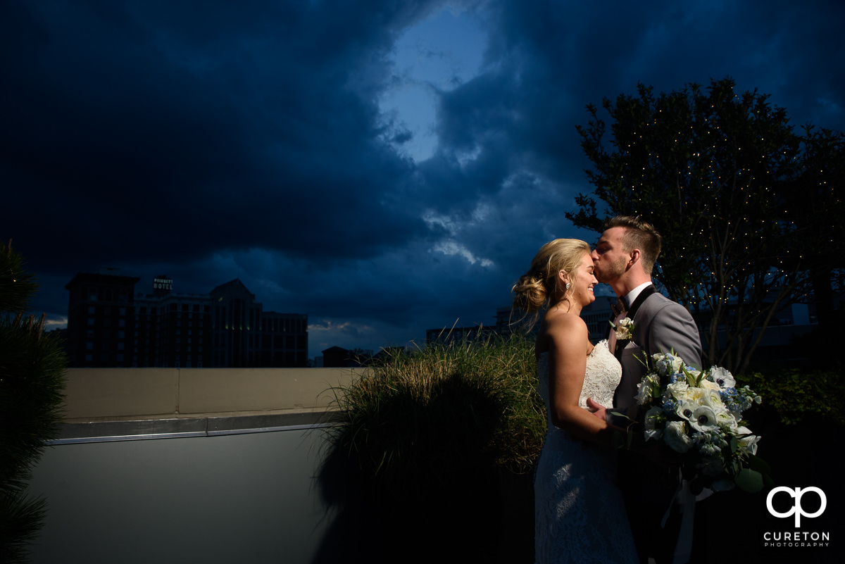 Groom kissing his bride on teh forehead after their wedding on the rooftop at Avenue in downtown Greenville,SC.