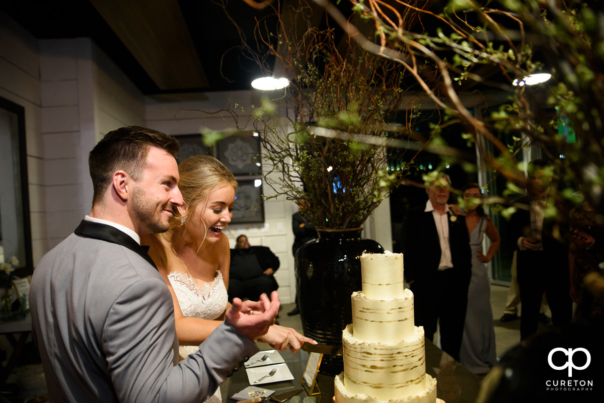 bride and groom laughing while cutting cake.