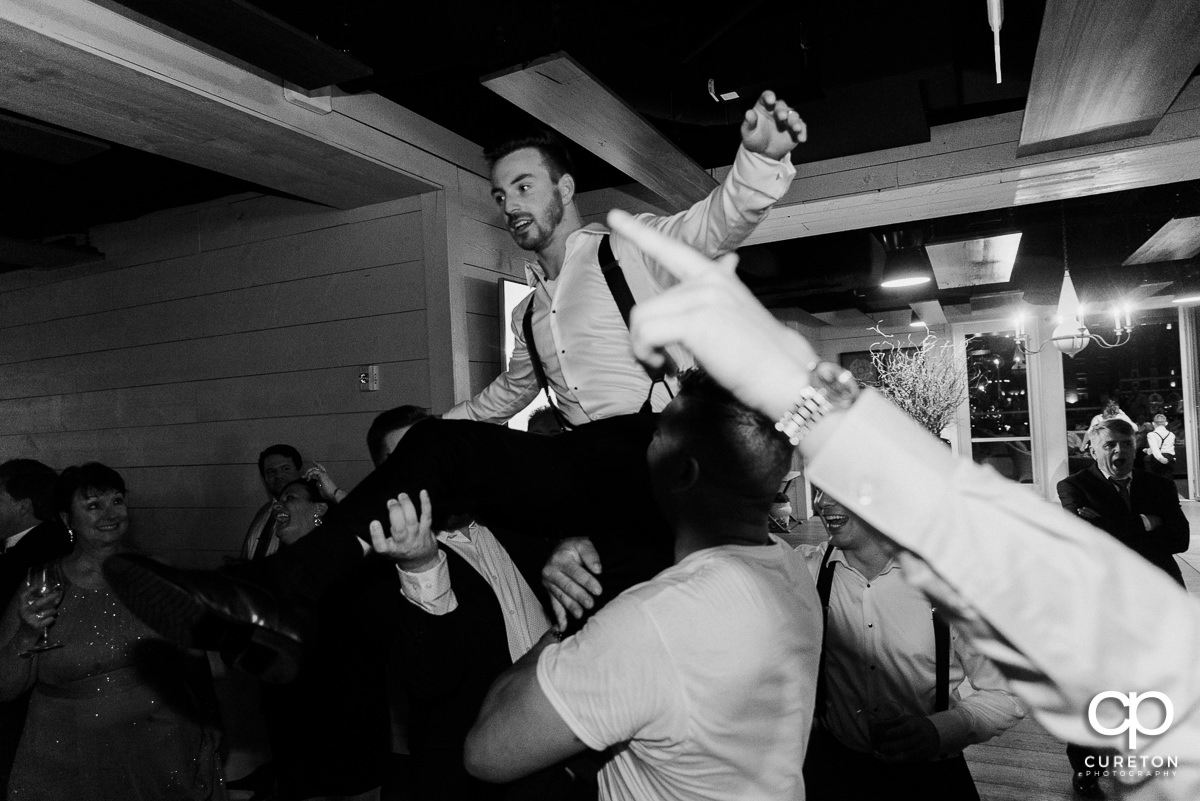 Groom being lifted above the dance floor at his wedding reception.