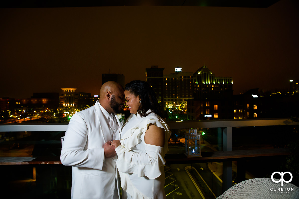 Bride and groom kissing with the night skyline of Greenville in the background.