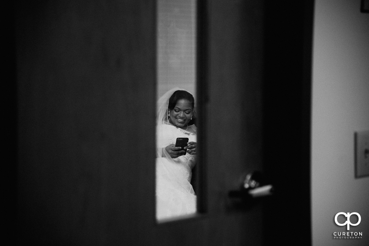 Bride texting and smiling though a window before the wedding ceremony.