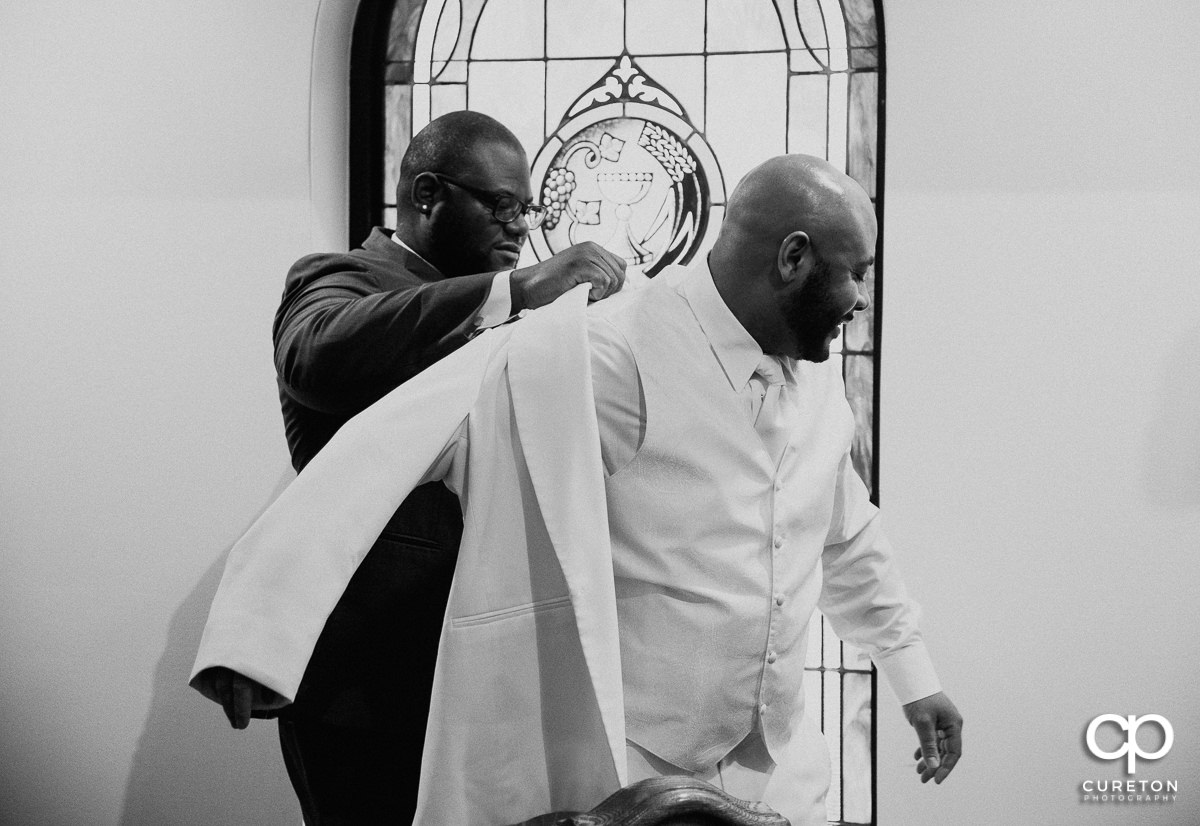 Groom getting helped into his jacket.