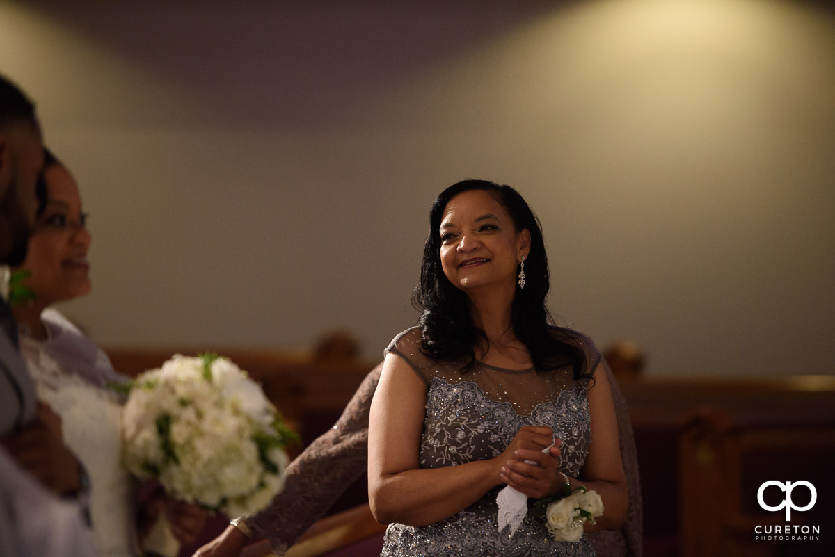 Bride's mother smiling as her daughter is walked down the aisle.