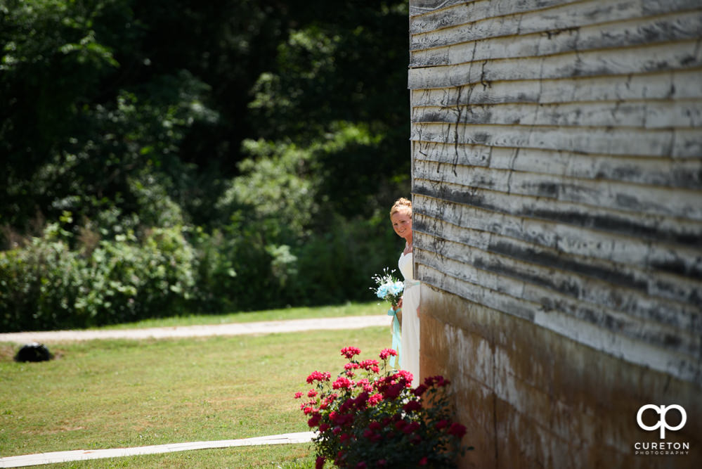 Bride peeking around the corner of the barn to see her groom.