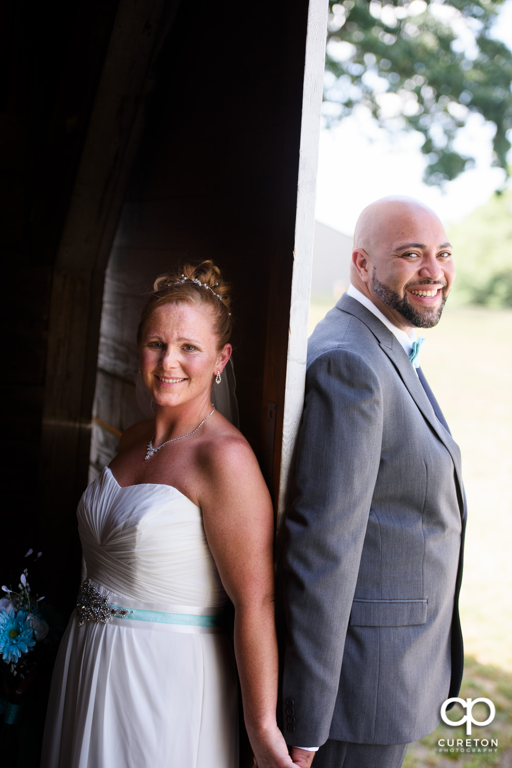 Bride and groom holding hands on each side of a barn door.