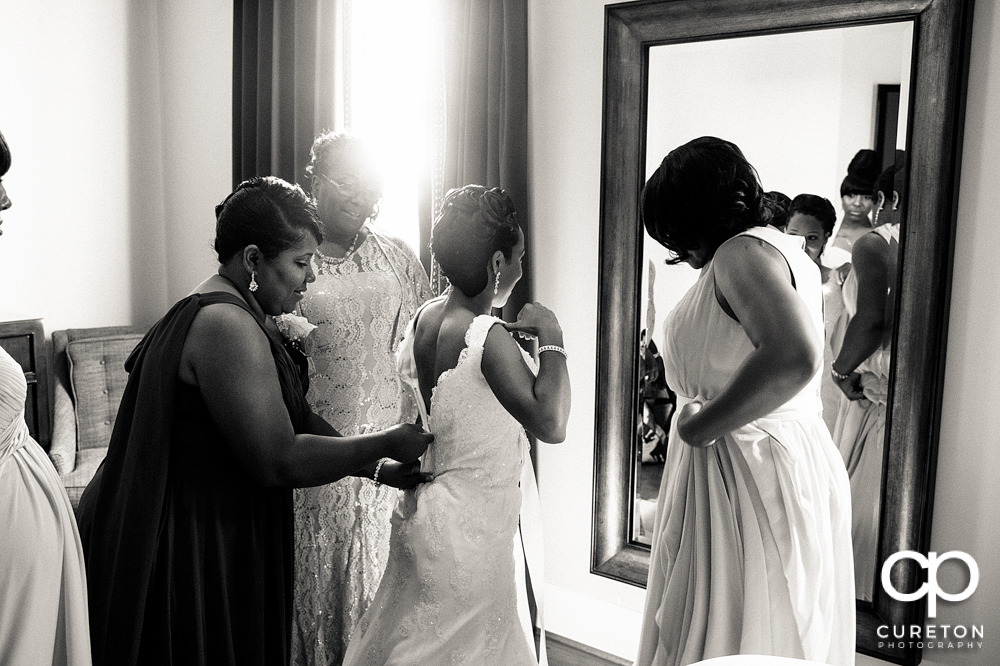 Bride putting on her dress with her mom and grandmother.