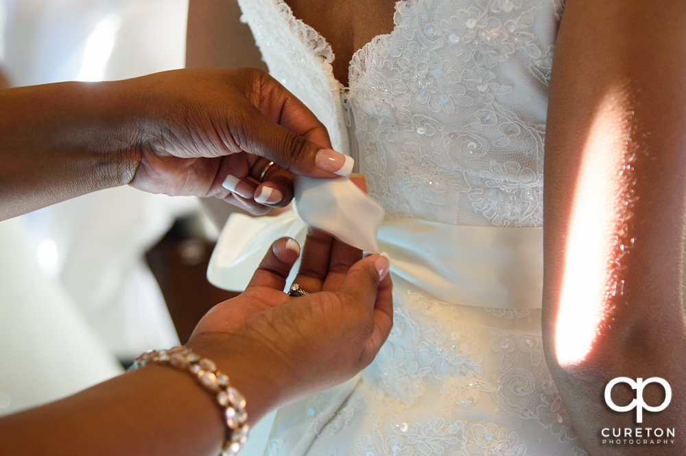 Mother of the bride zipping the bridal dress up.