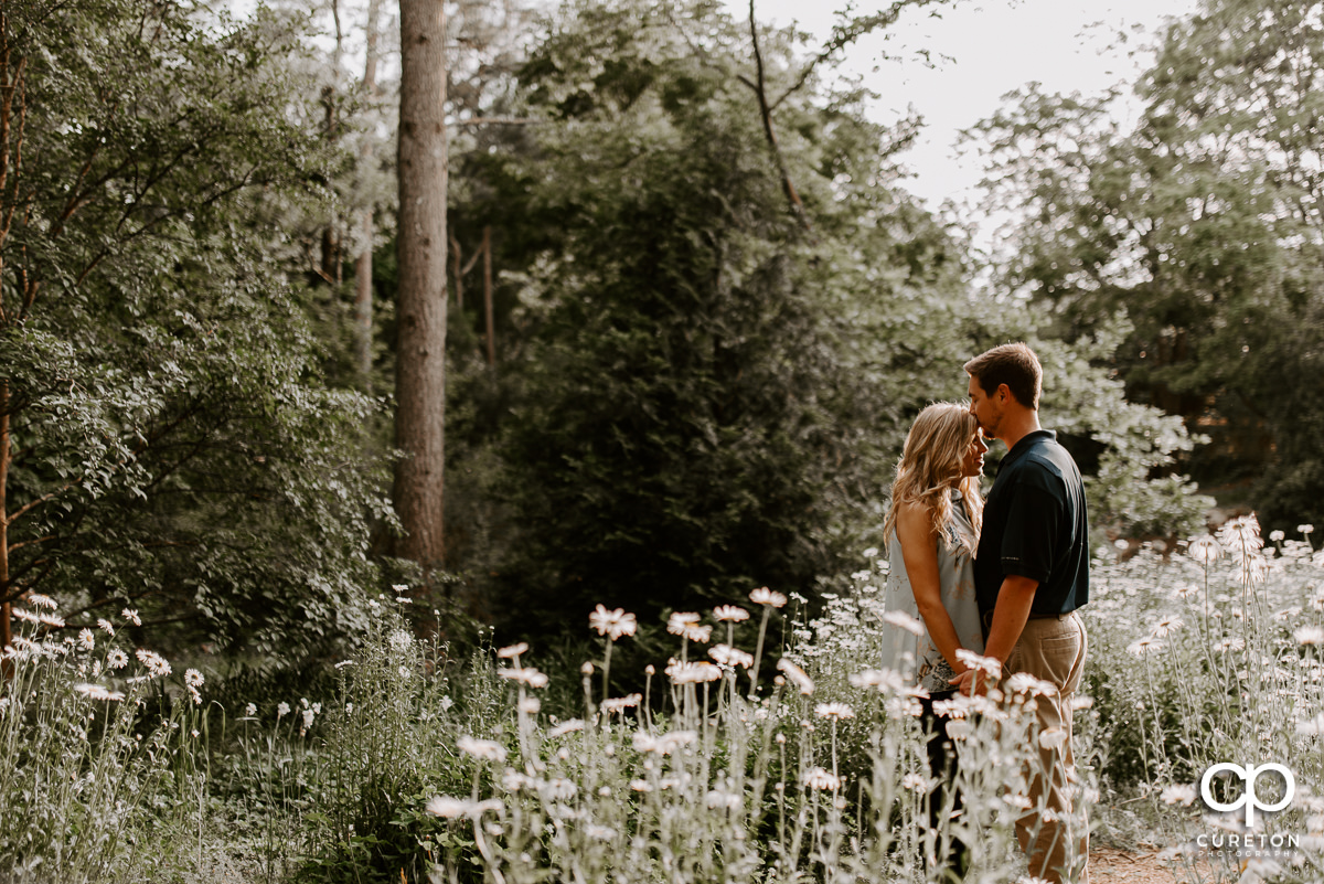 Future groom kissing his bride on the forehead in a field of wildflowers during their Botanical Gardens engagement session in Clemson,SC.