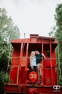 Bride and groom standing on a red train car during their Clemson Botanical Gardens engagement session.