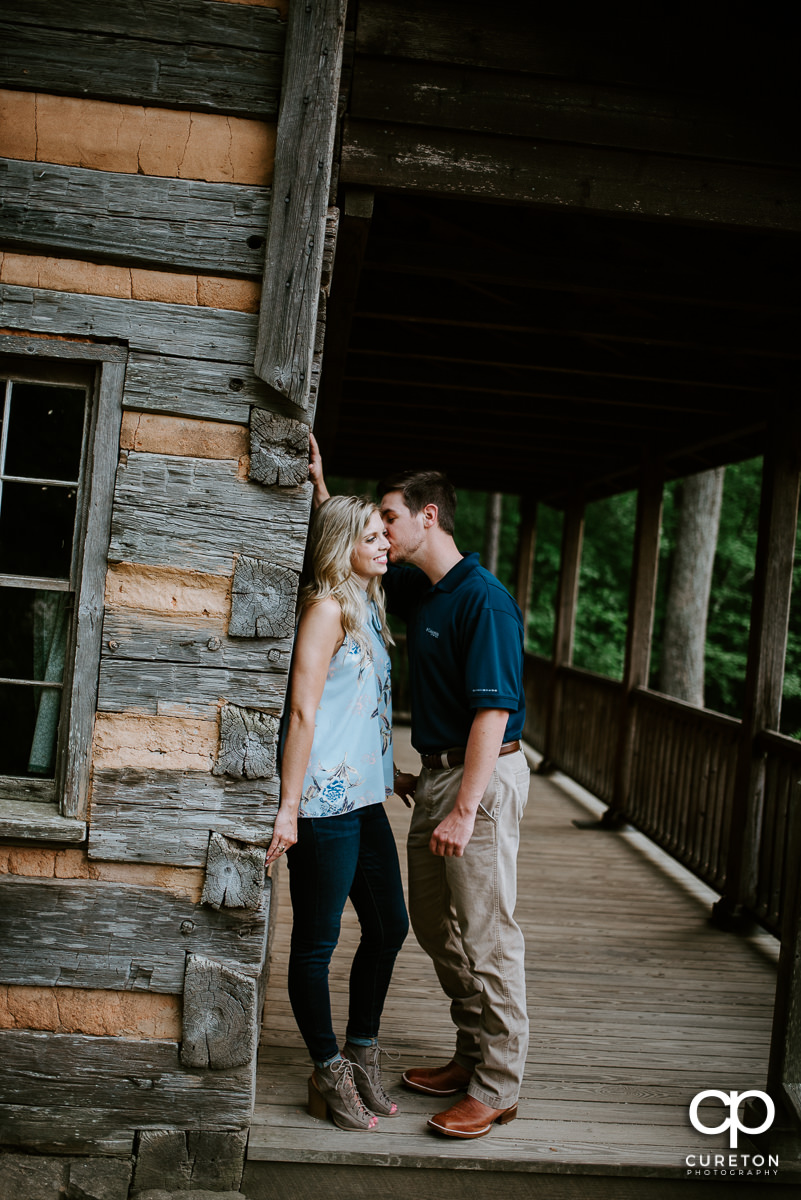Man kissing his fiancee on the cheek at the Hunt Cabin at the Botanical Gardens in Clemson.