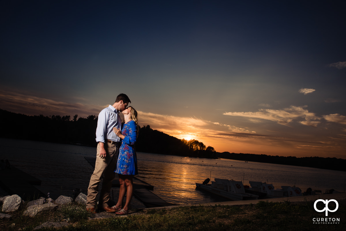 Future bride kissing her groom at sunset by the lake in Clemson.