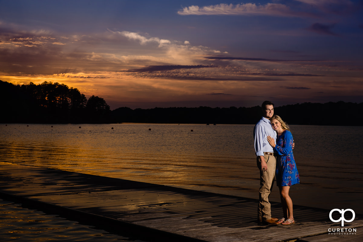 Engaged couple standing on a dock by the lake on the Clemson University campus.