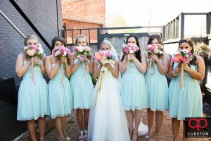 Brie and bridesmaids holding flowers over their faces..