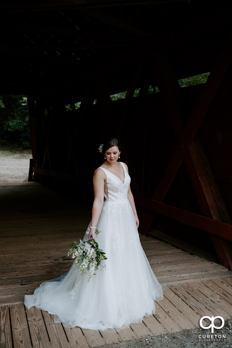 Bride looking at her flowers in an antique wooden covered bridge.