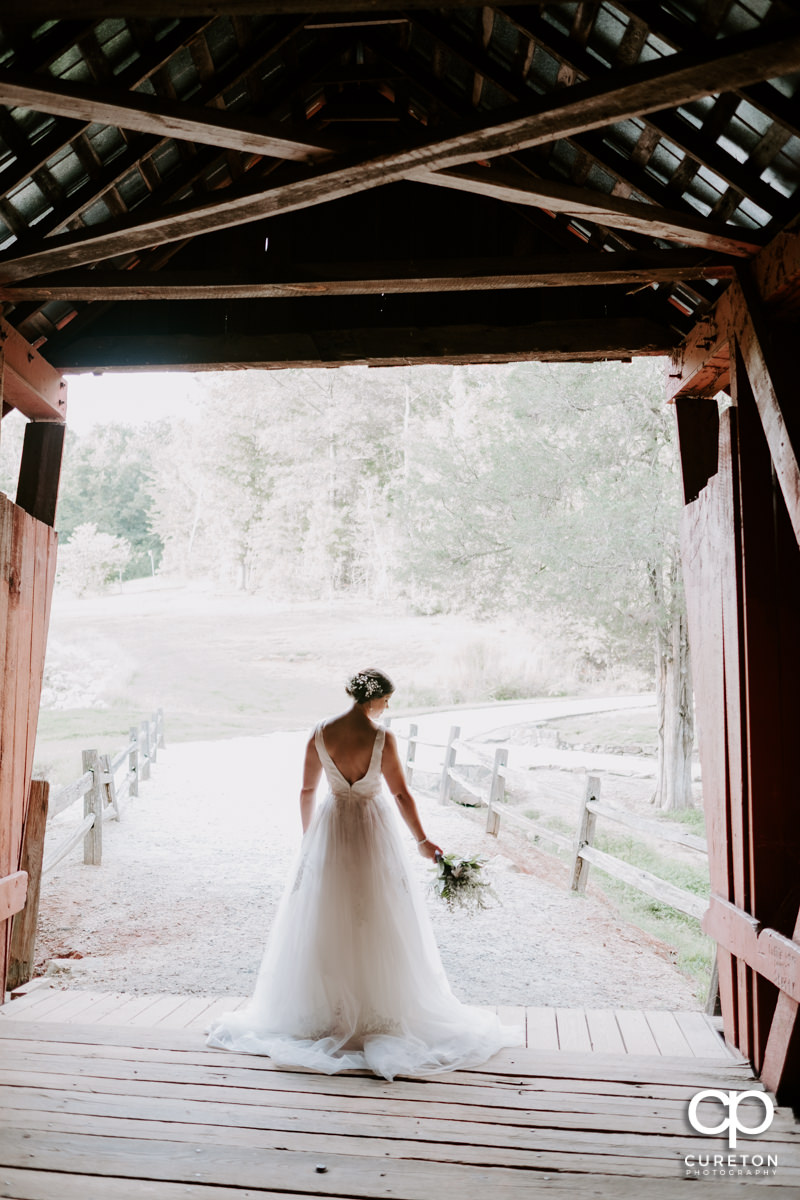 Bride holding her flowers as she walks out of an antique covered bridge.
