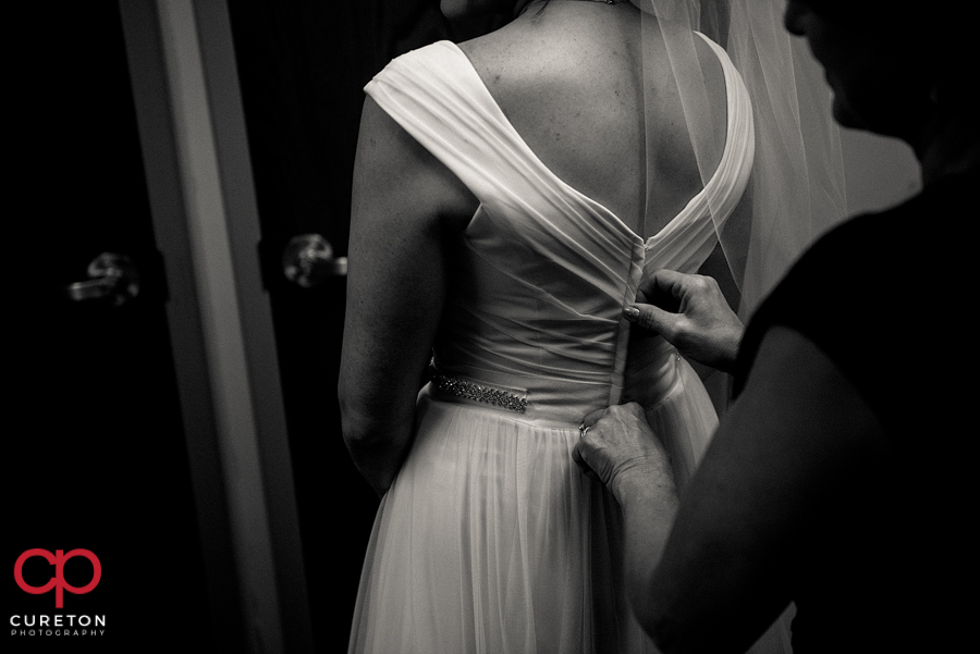 Bridesmaid zipping the back of the bride's dress.