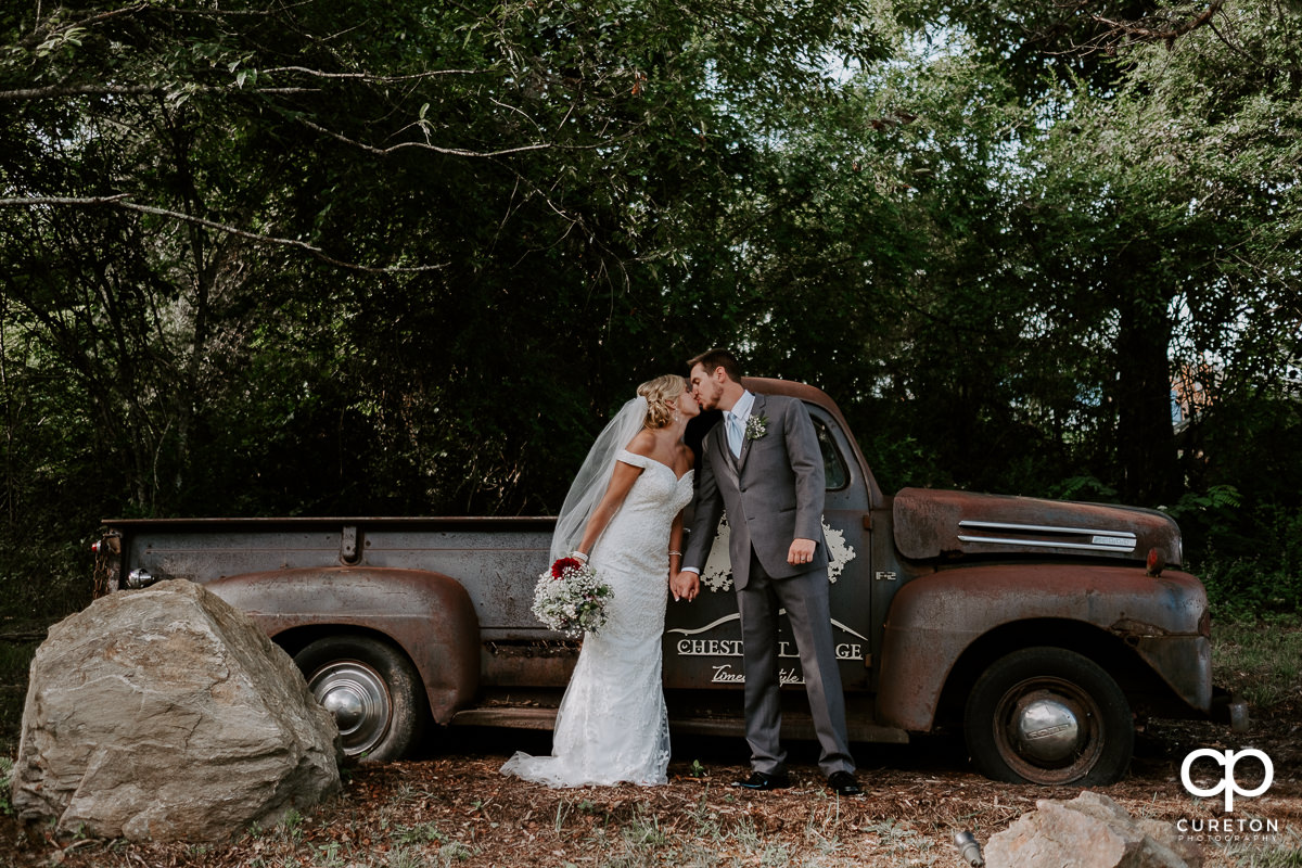 Bride and groom kissing in front of a rustic vintage pickup truck after their wedding at Chestnut Ridge in Canton,NC.